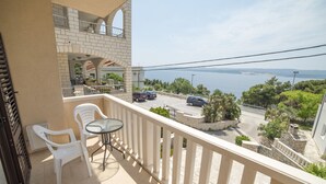 A balcony with a table and chairs, overlooking a street and a body of water. - Apartments Pavla i Niko (Lokva Rogoznica)