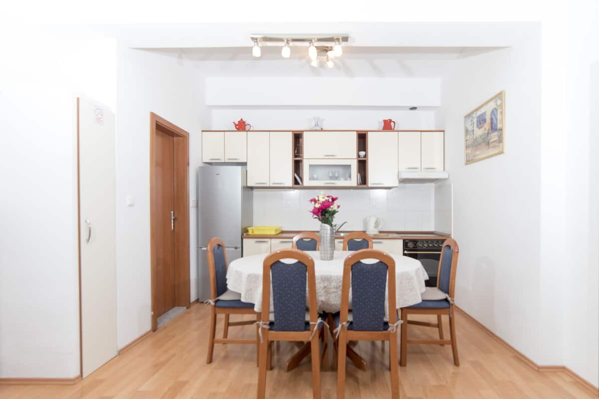 A compact kitchen with white cabinets, a microwave, and a stove. There is a dining table with four chairs and a vase with flowers.