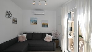 Una sala de estar moderna con un sofá gris oscuro, dos cojines, una planta en maceta y obras de arte en las paredes.