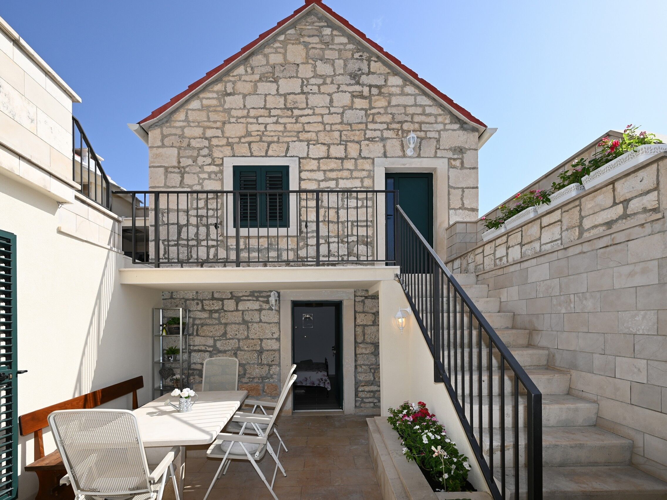 A stone building with a balcony, a staircase, and a patio area with a table and chairs.