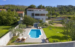 A modern two-story building with a swimming pool, surrounded by a well-maintained lawn and trees. - House Anavi (Tugare)
