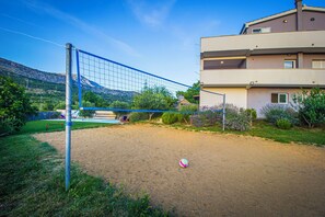 A sandy outdoor volleyball court with a net, surrounded by greenery and a building. - House Anavi (Tugare)