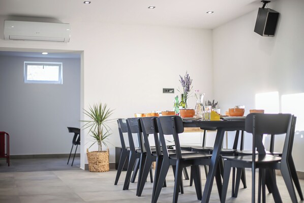 A modern dining area with a round table, black chairs, and a potted plant. - House Anavi (Tugare)