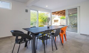 A dining area with a table and chairs, large windows, and a view of the outdoors. - House Anavi (Tugare)