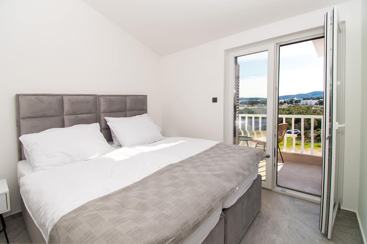 A bedroom with a large bed, a balcony with a view, and a sliding glass door.