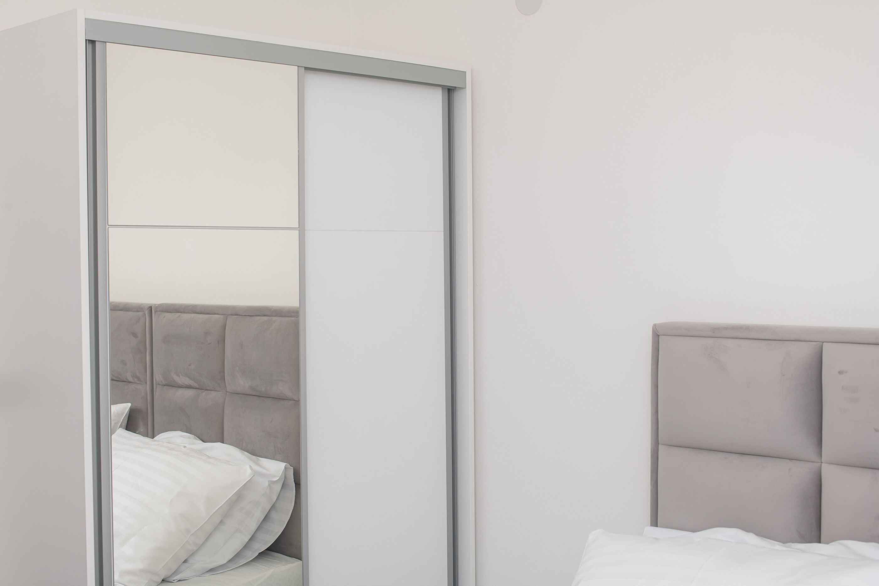 A bedroom with a bed, a wardrobe with a mirror, and a headboard.