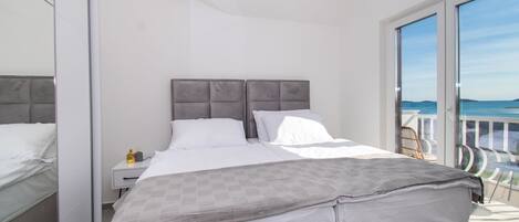 Un dormitorio moderno con una cama grande, una mesita de noche y vistas al mar desde un balcón.