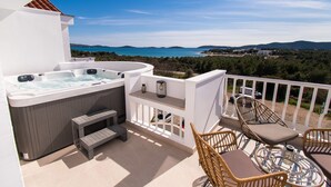 A balcony with a hot tub, wicker chairs, a glass table, and a scenic view of the sea and hills. - Apartments Valeva Exclusive (Sibenik)