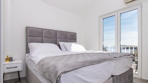 A modern bedroom with a large bed, a nightstand, and a view of the outdoors through a sliding glass door. - Apartments Valeva Exclusive (Sibenik)