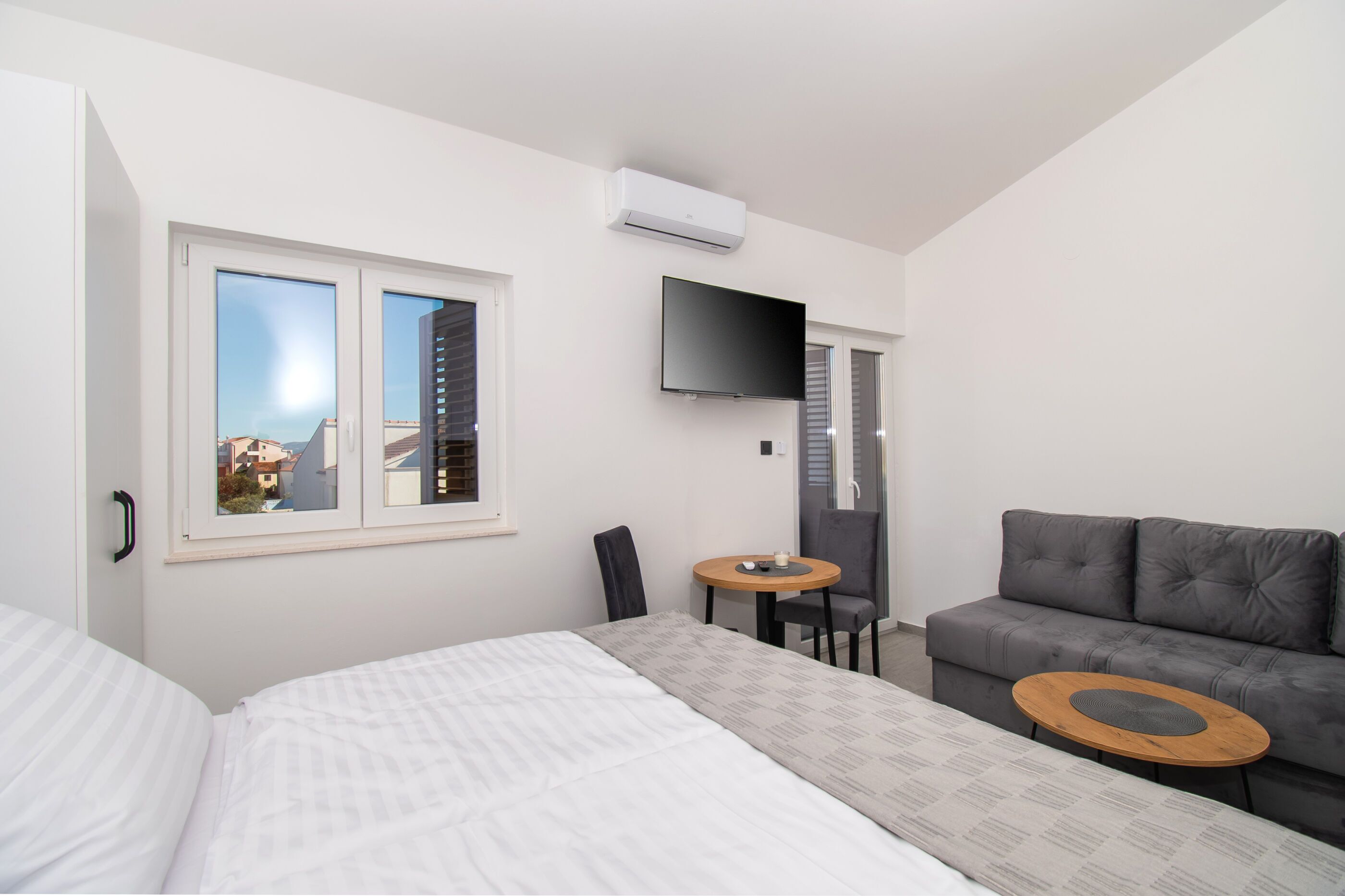 Une chambre d’hôtel moderne, équipée d’un lit, d’un canapé gris, d’une petite table ronde et d’un téléviseur fixé au mur.