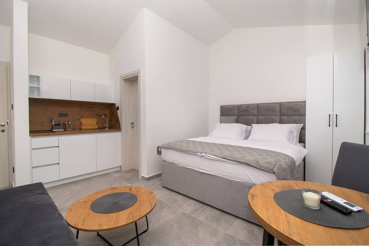 A modern bedroom with a bed, bedside tables, a small kitchenette, and a wardrobe.