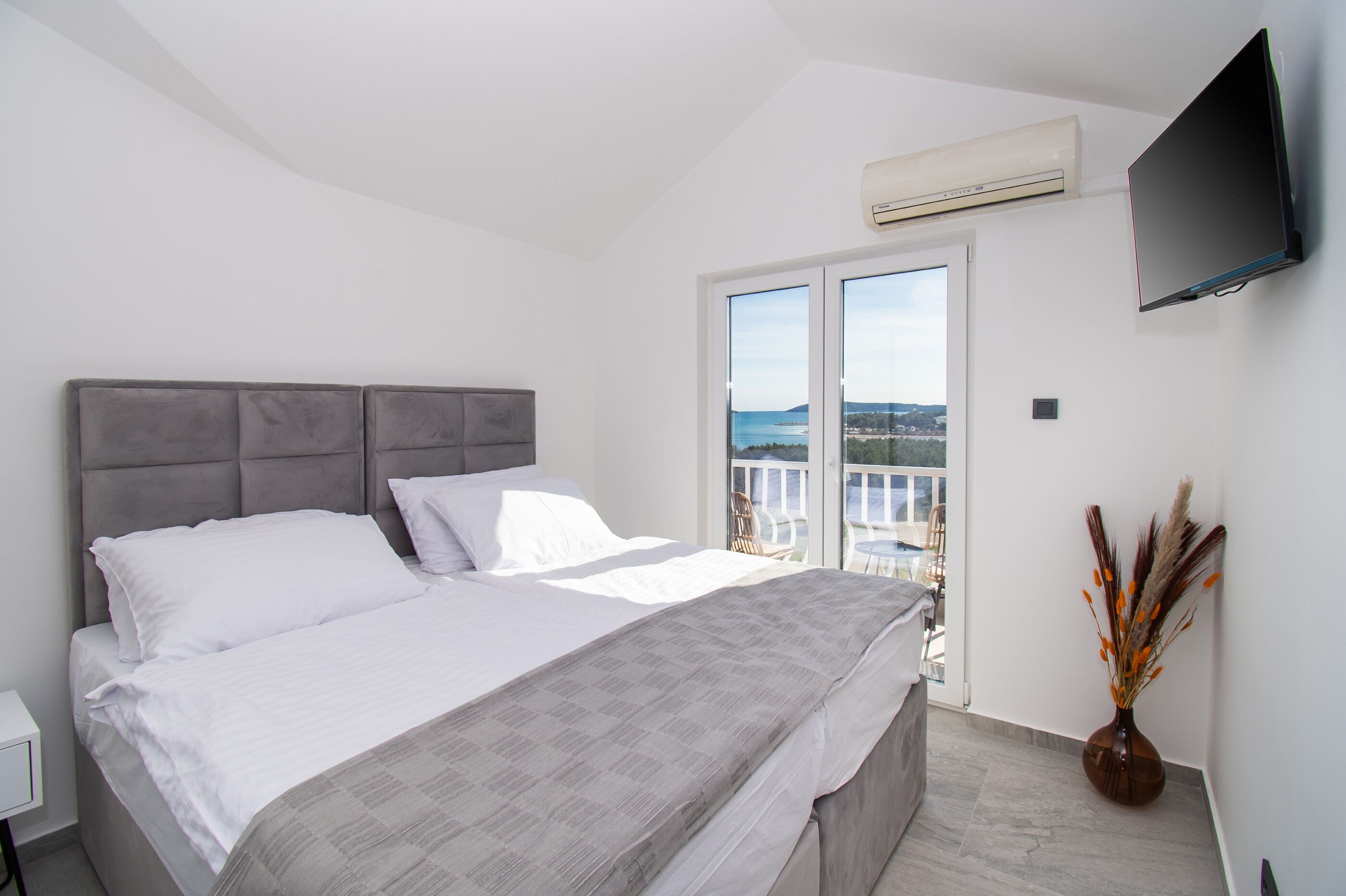 A bedroom with a large bed, a flat-screen TV mounted on the wall, and a view of the outdoors through a sliding door.