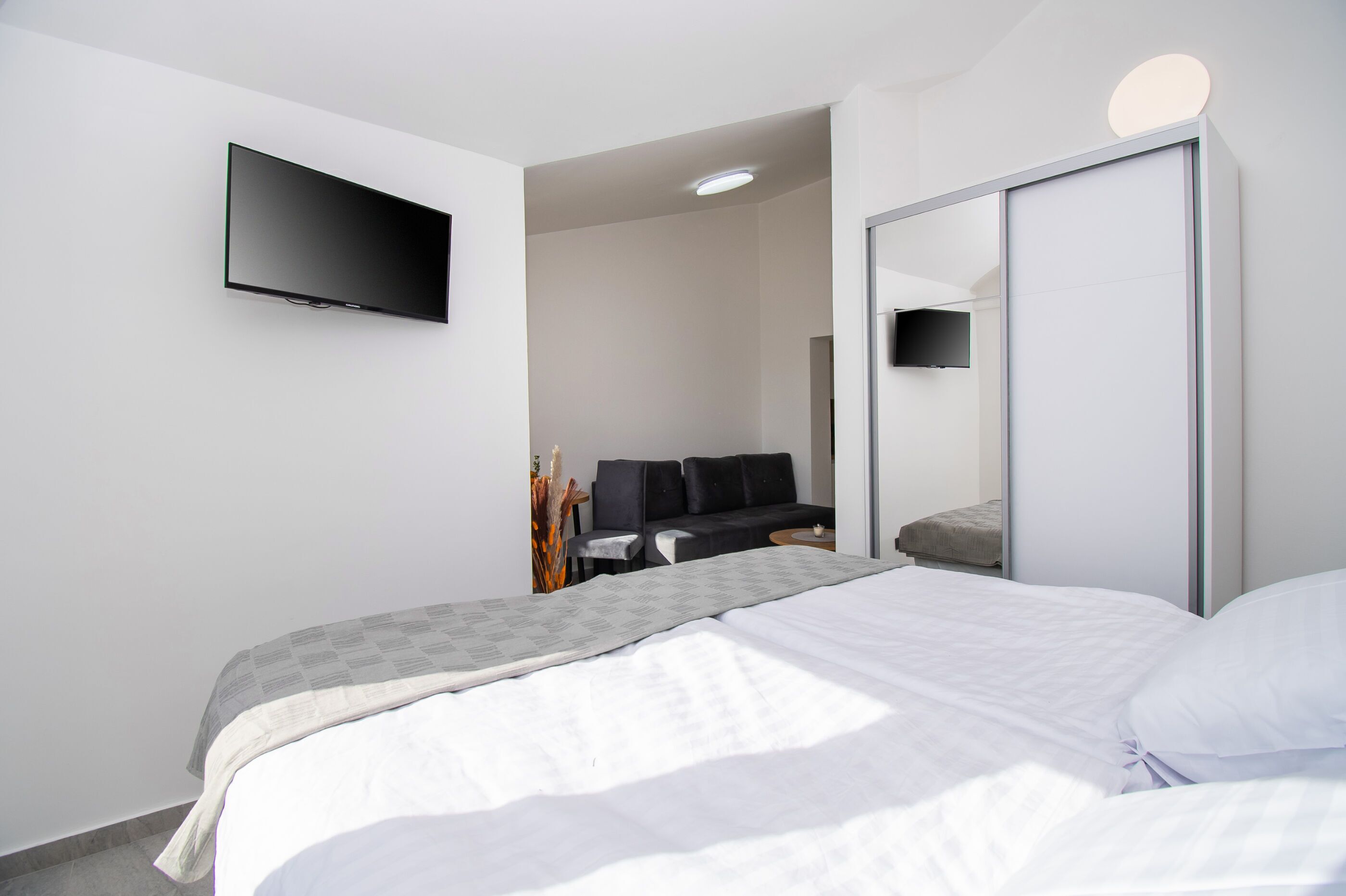 Quarto de hotel moderno com uma cama grande, televisão de tela plana na parede, sofá e espelho.