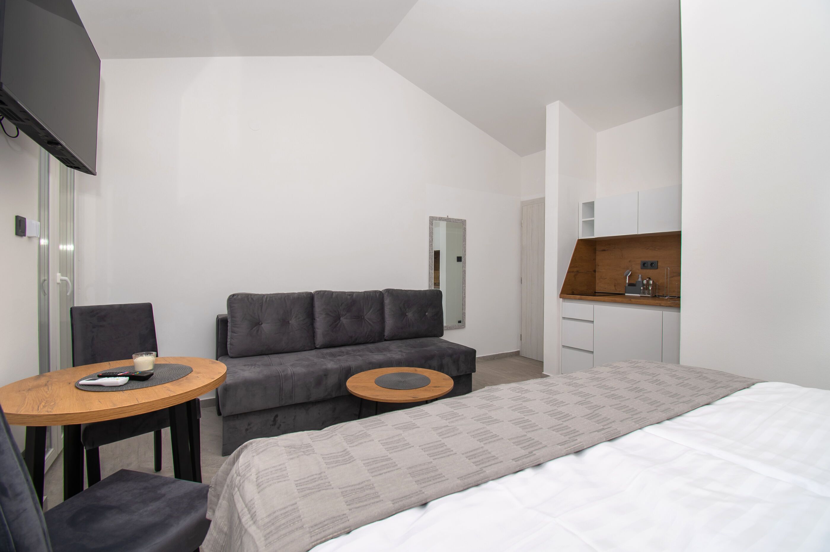 Una camera d'albergo moderna con un divano, un piccolo tavolino rotondo, un letto, una scrivania in legno e una TV a parete.