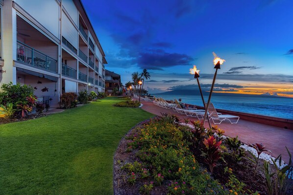 A hotel with a poolside area, lounge chairs, and a view of the ocean at dusk.