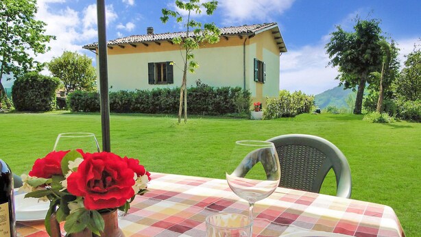 A table set outdoors with a vase of flowers, a wine glass, and plates.