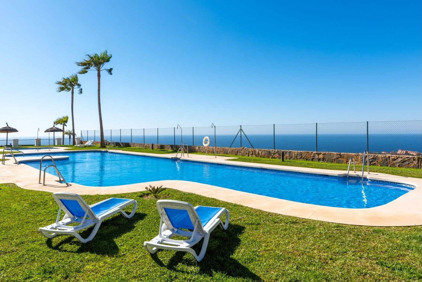 Una piscina amb dues gandules, una paret de pedra i vista a l'oceà.