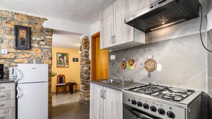 Una cucina con piano cottura a gas, forno integrato e frigorifero. Sullo sfondo, un muro in pietra e una porta in legno.