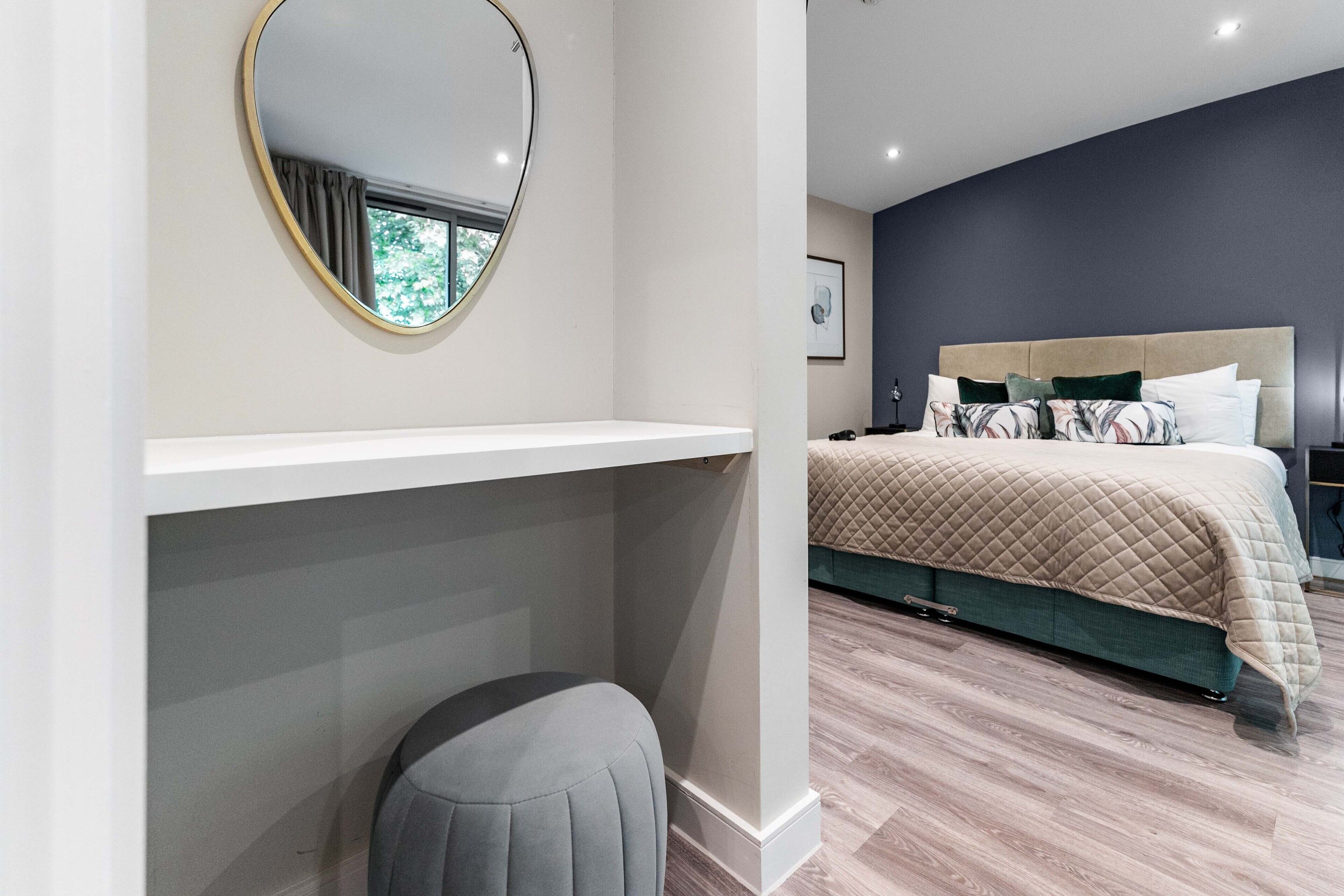 Un dormitorio con cama, mesita de noche, espejo y ventana.