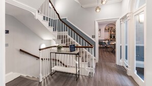 A spacious hallway with a wooden staircase, a dining area, and a view of the outdoors. - The Regent Aparthotel (Cambridge)