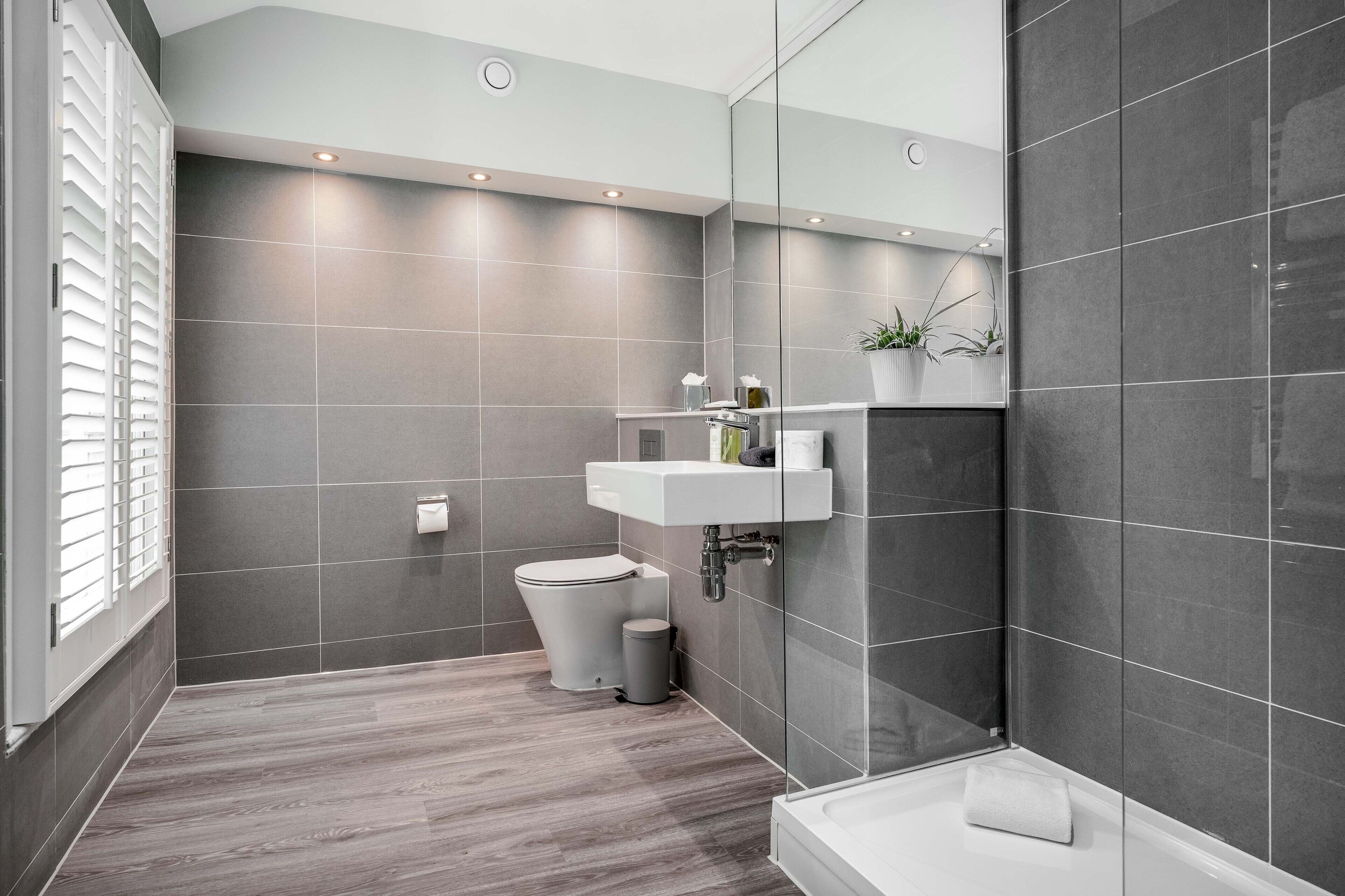 Un baño moderno con azulejos grises, inodoro, lavamanos y zona de ducha.