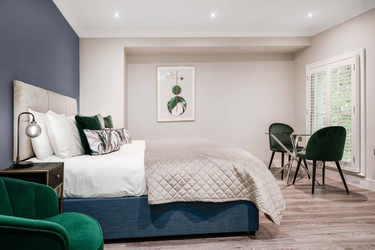 Une chambre à coucher avec un lit, un bureau, une chaise et une fenêtre avec des stores.