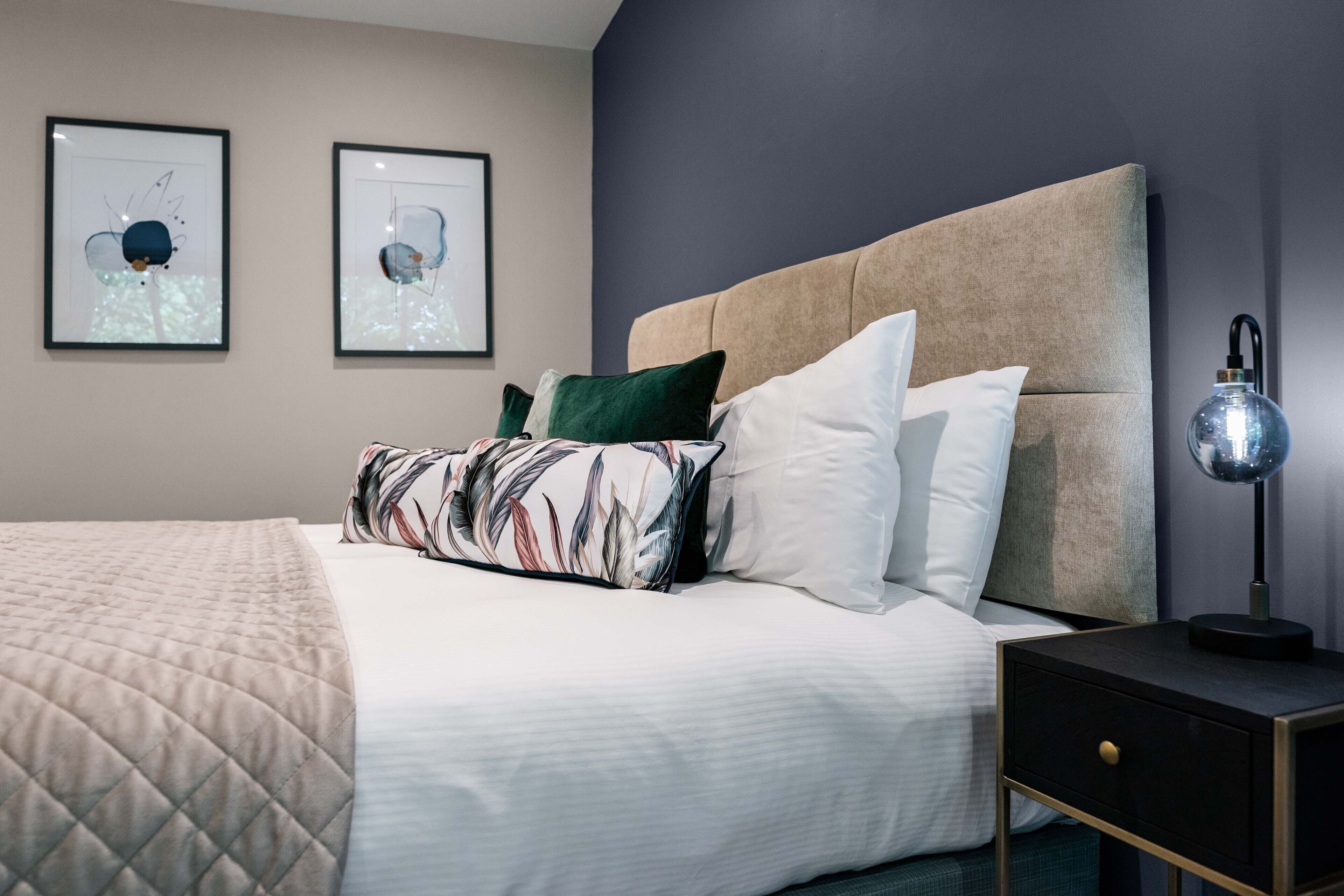 A neatly made bed with a quilted blanket, a headboard, and a bedside table with a lamp.