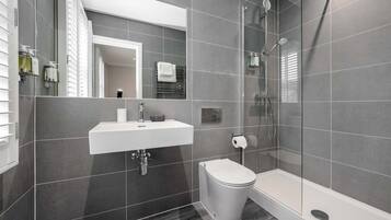 Een moderne badkamer met een wit wastafelmeubel, toilet en douche.