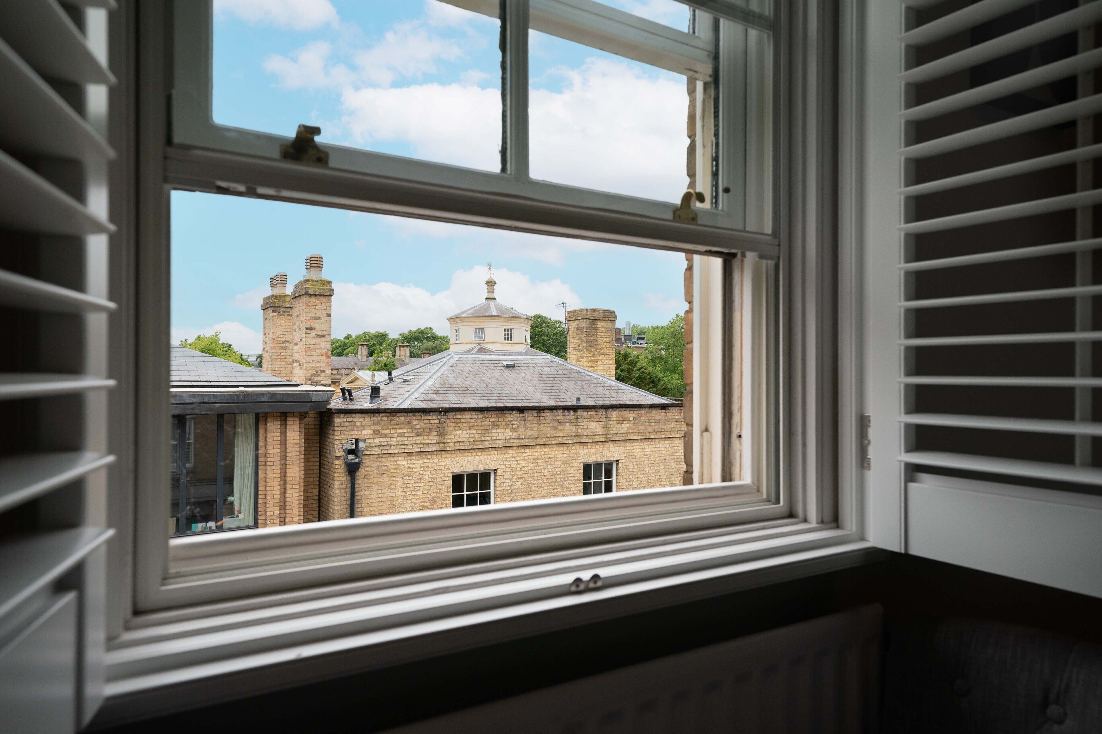 A window with a view of a building with brick walls and chimneys.
