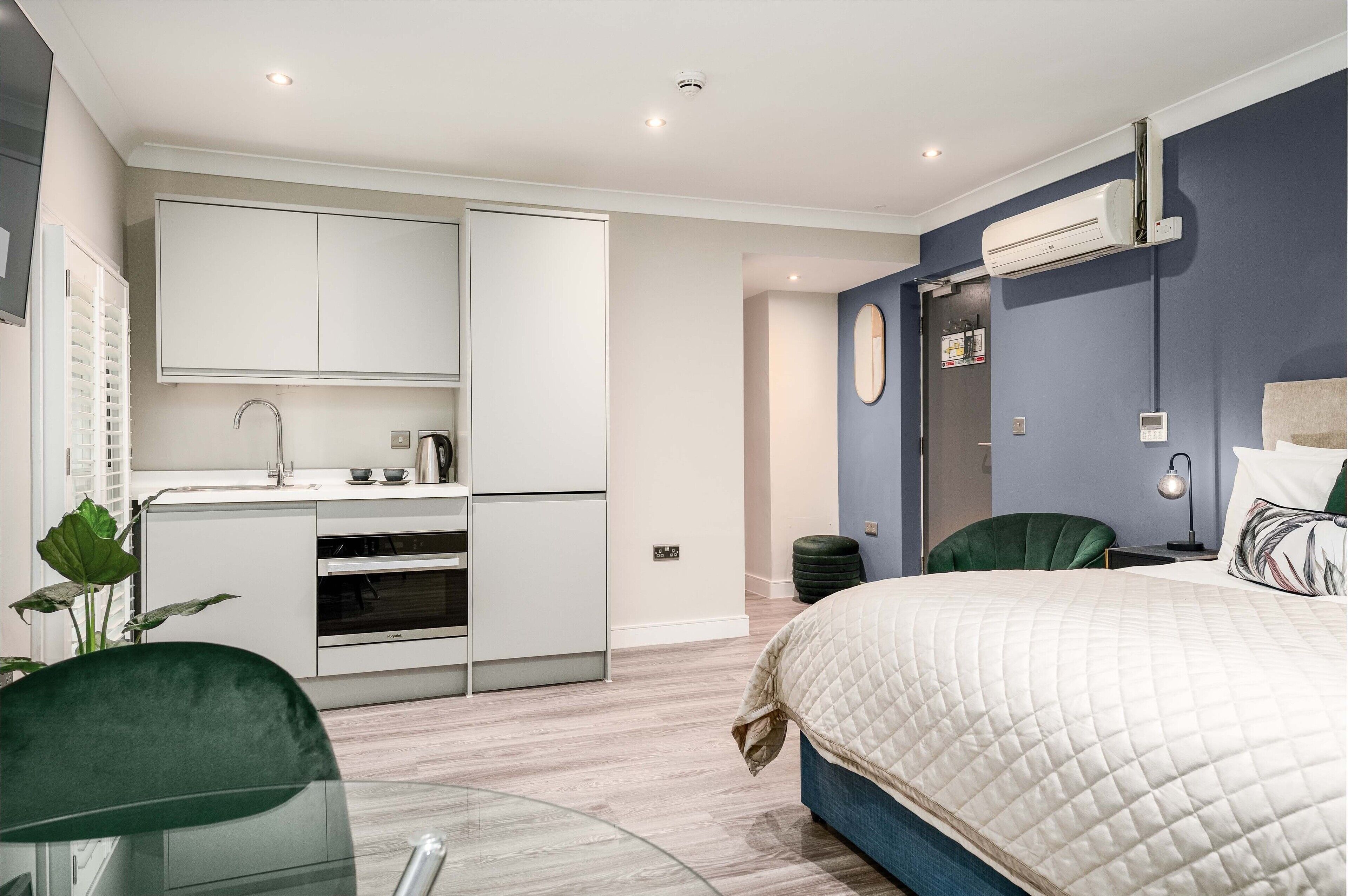 A modern bedroom with a bed, a desk, and a kitchenette.