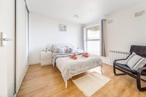 A bedroom with a bed, a nightstand, a chair, and a window.