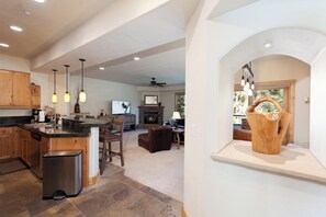 A spacious kitchen with a stone countertop, wooden cabinets, and a central island. There is a fireplace, a dining area with chairs, and a large window providing natural light. - Largest Black Bear Townhome - Private Hot Tub - EV Charger - Ski Shuttle (Durango)