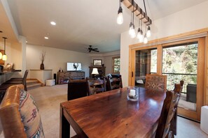 A spacious living room with a wooden dining table, comfortable seating, a fireplace, and a large window offering a view of the outdoors. - Largest Black Bear Townhome - Private Hot Tub - EV Charger - Ski Shuttle (Durango)