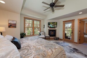 A spacious bedroom with a large bed, a fireplace, a ceiling fan, and large windows offering a view of the outdoors. - Largest Black Bear Townhome - Private Hot Tub - EV Charger - Ski Shuttle (Durango)