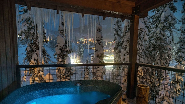 Un bain à remous avec vue sur un paysage enneigé et des bâtiments en arrière-plan.