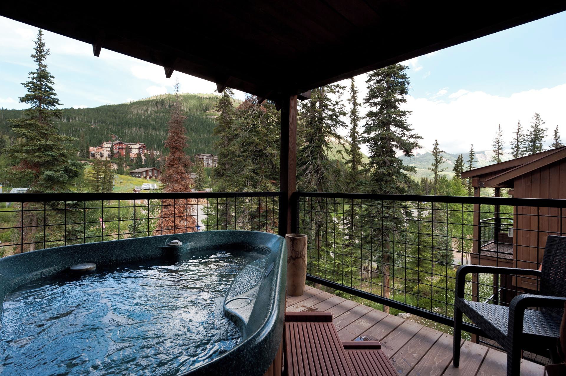 A hot tub on a wooden deck with a view of a mountainous landscape and a building in the background.