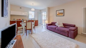 A modern apartment with a dining area, kitchen, living room, and a large TV. - Casa Margherita Few Minutes From Lake (Riva del Garda)