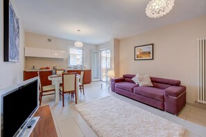 A modern apartment with a dining area, kitchen, living room, and a large TV.