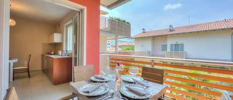 A dining area with a table set for four, a kitchen in the background, and a balcony with a view of the neighborhood.