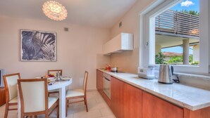 A modern kitchen with a dining area, a large window with a view, and a pendant light. - Casa Margherita Few Minutes From Lake (Riva del Garda)