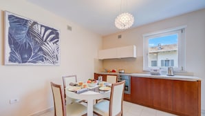A modern kitchen with white cabinets, a dining table with chairs, a pendant light, and a large window. - Casa Margherita Few Minutes From Lake (Riva del Garda)