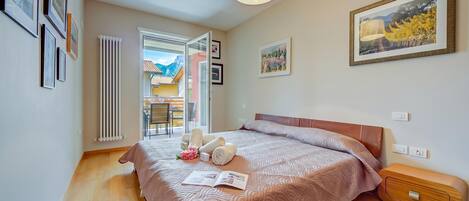 A bedroom with a bed, a radiator, a window, and a door leading to a balcony.