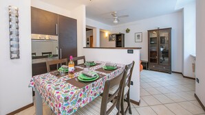 A dining area with a table set for four, a modern kitchen in the background, and a ceiling fan. - Casa Azzurra 150m From Lake Garda (Riva del Garda)
