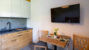 A modern kitchen with wooden cabinets, a herringbone backsplash, and a built-in TV above the dining table. - Aparthotel pod Stokiem (Szczyrk)