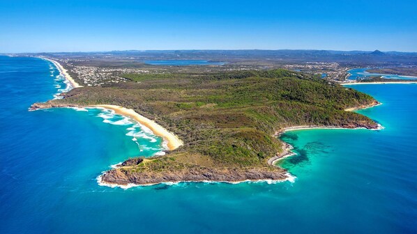 Vista aérea de una zona costera con playa, abundante vegetación y mar azul cristalino.