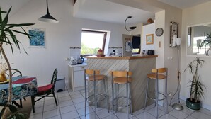 A modern kitchen with a bar area, bar stools, and a dining table with chairs. - Beautiful duplex with sea view balcony at Le Cabellou in Concarneau  (Concarneau)