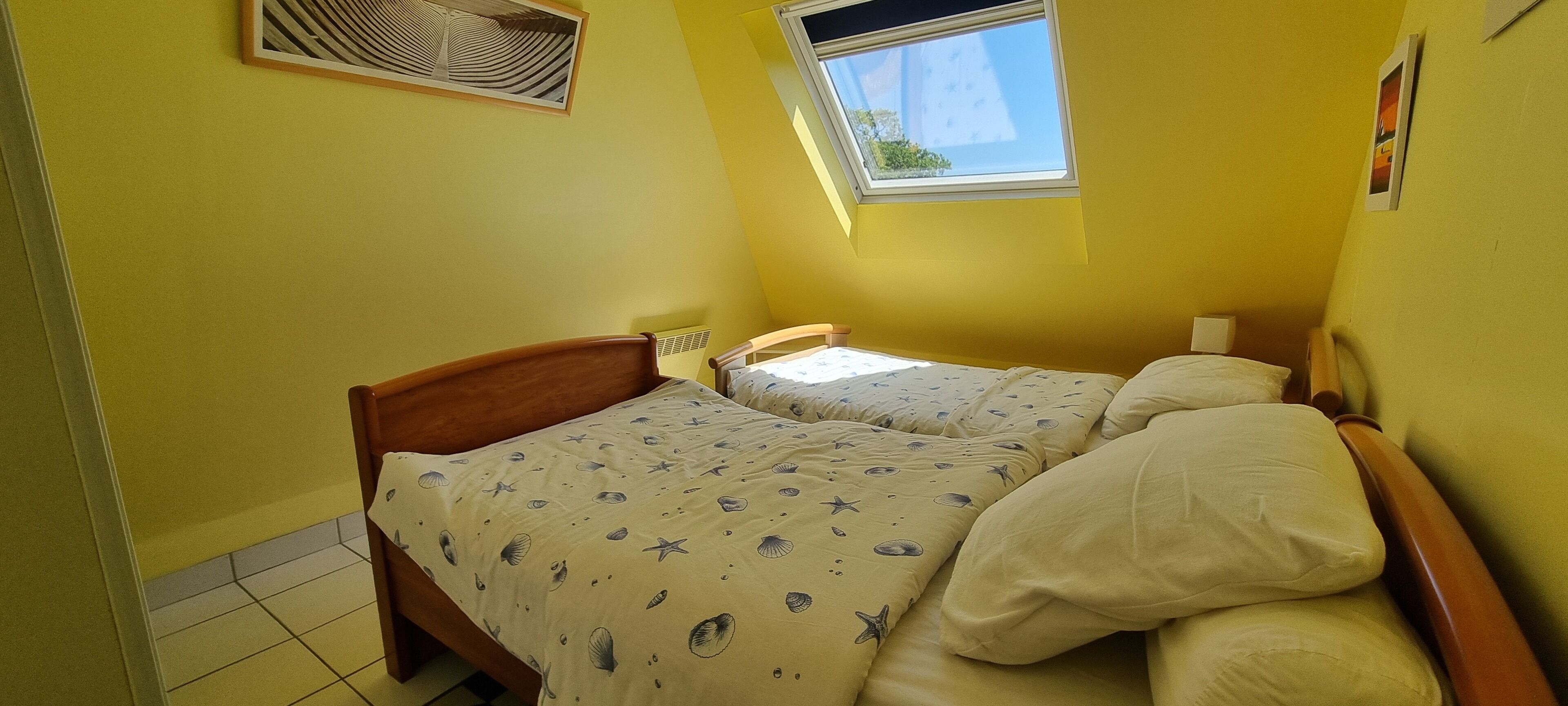 Une petite pièce avec deux lits, une fenêtre et un radiateur.