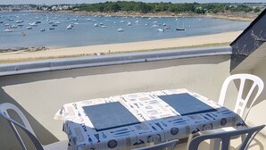 A balcony with a table and chairs overlooking a beach with boats. - Beautiful duplex with sea view balcony at Le Cabellou in Concarneau  (Concarneau)