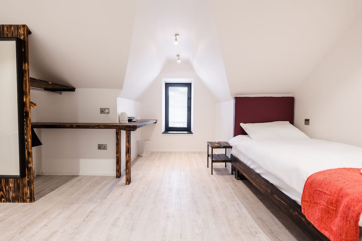 A bedroom with a bed, a desk, a window, and a mirror.