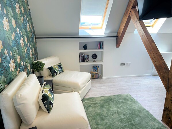 A modern living room with a white sofa, green patterned cushions, a small plant, and a bookshelf with books and a globe. - Cardiff Arms Bistro and Hotel (Treorchy)